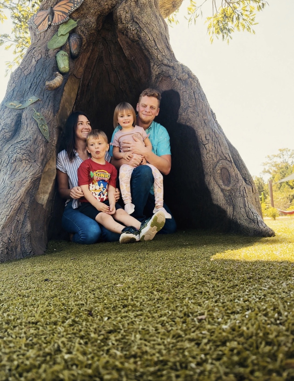 Anna Marie with her husband and two children in front of a large tree