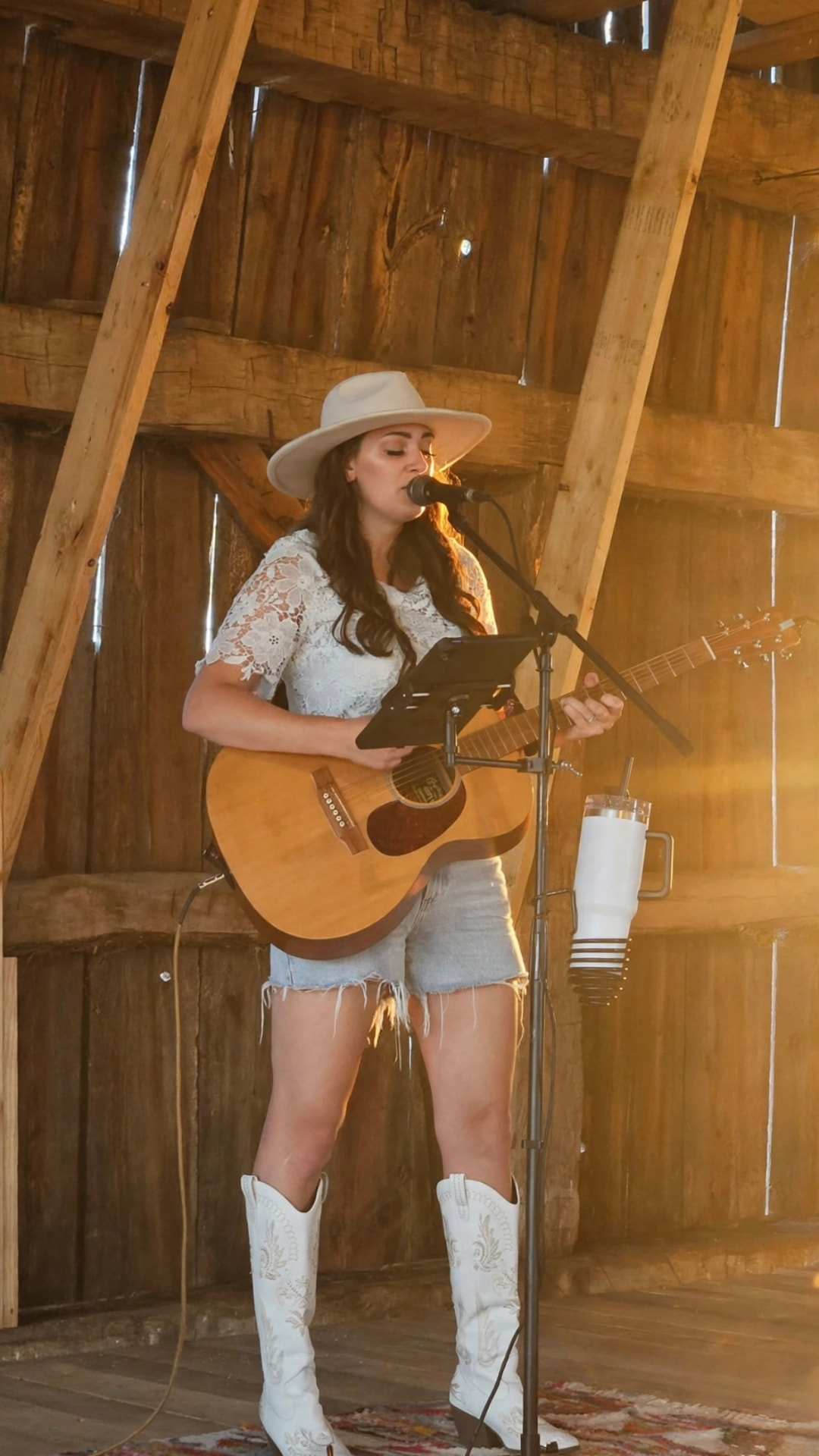 Anna Marie in a white hat performing with guitar in a rustic barn