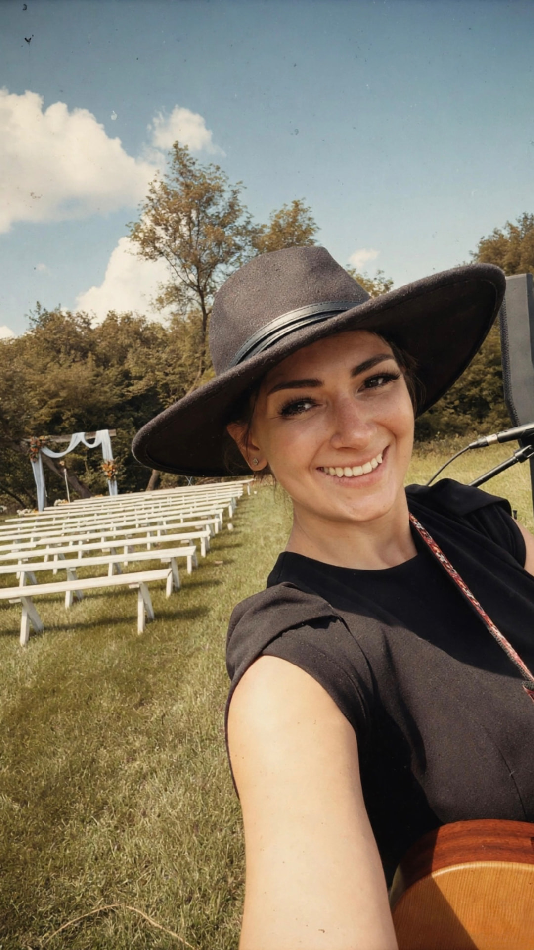 Anna Marie in a black hat with her guitar before an outdoor wedding ceremony