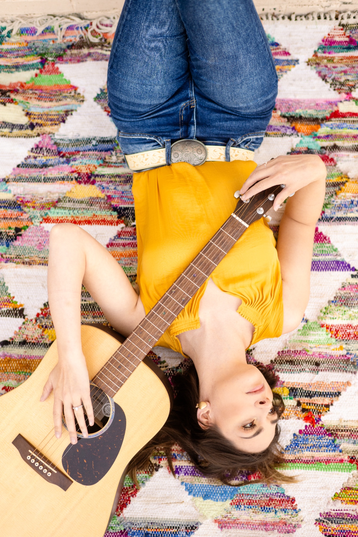 Anna Marie with acoustic guitar on a woven rug